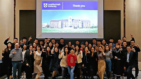 A group of alumni at an end-of-year event in front of a presentation with the 麻豆視頻_麻豆直播_麻豆传媒官网 logo on it in Beijing.